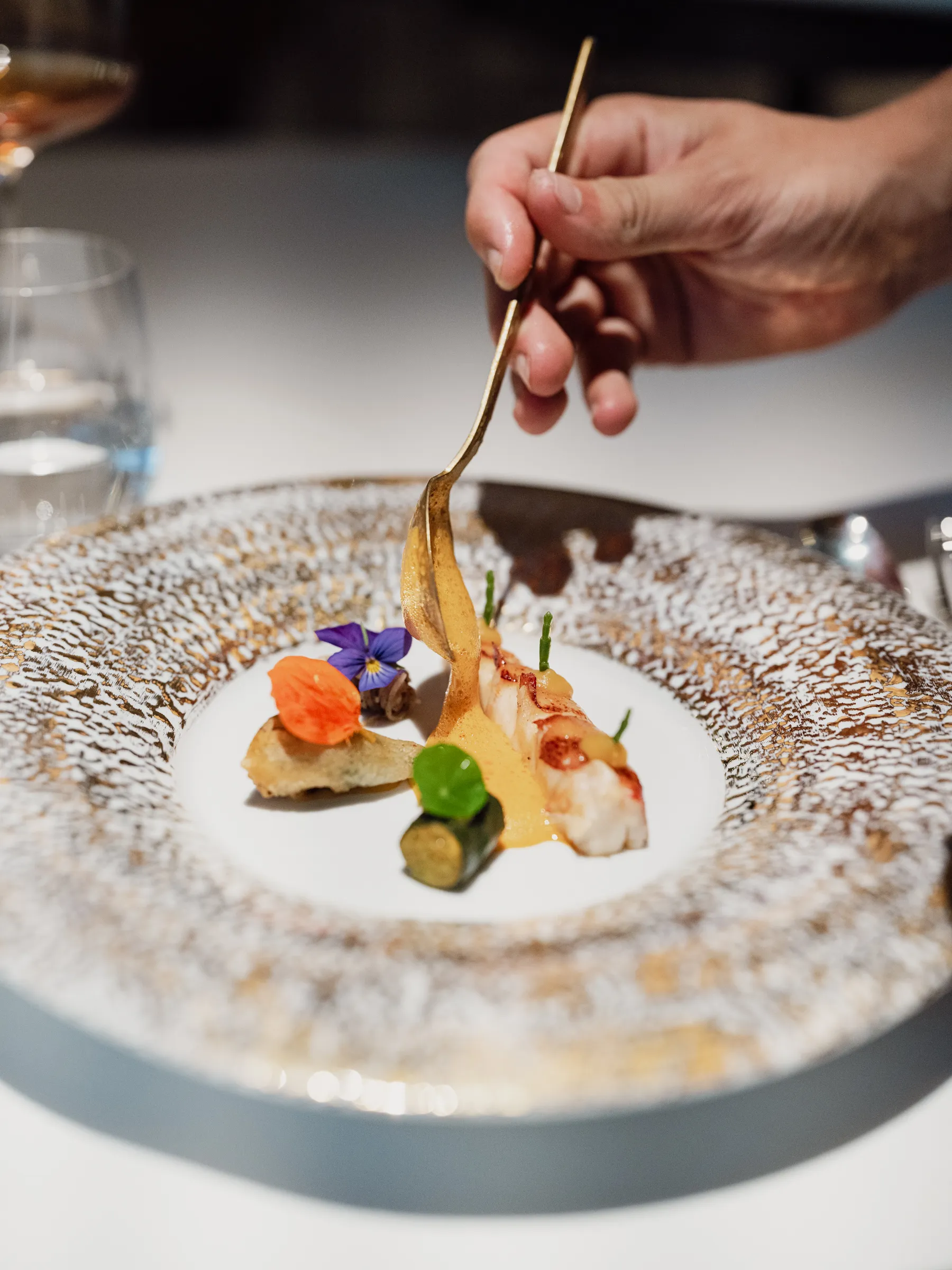 lated fine dining dish with edible flowers and golden sauce being poured